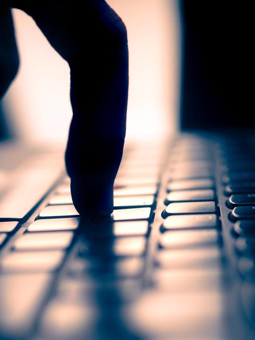 Finger tippt auf Tastatur, dunkle Umgebung und Gegenlicht