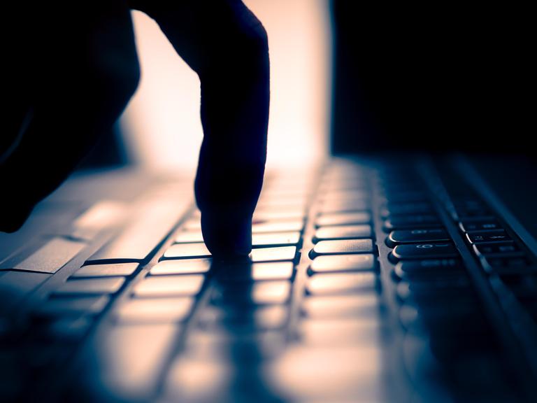 Finger tippt auf Tastatur, dunkle Umgebung und Gegenlicht