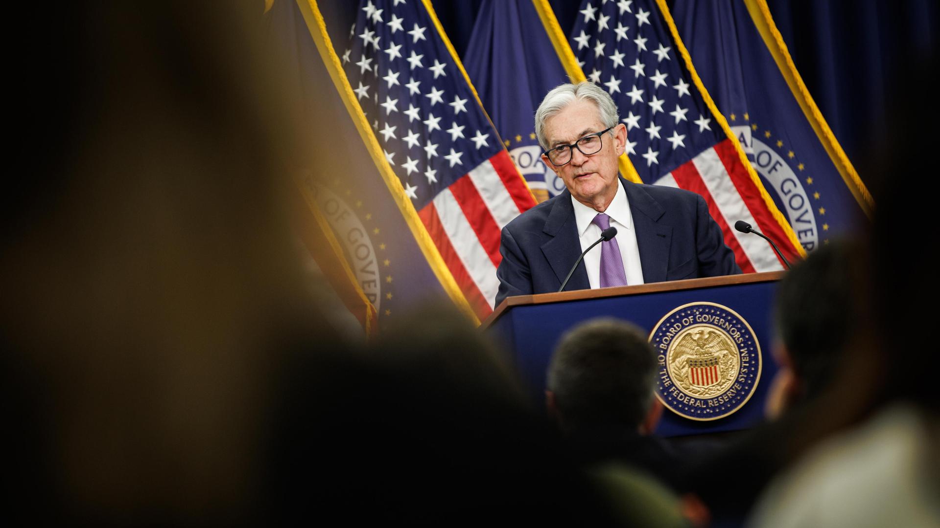 Jerome Powell steht hinter einem Rednerpult. Hinter ihm zwei US-Flaggen.