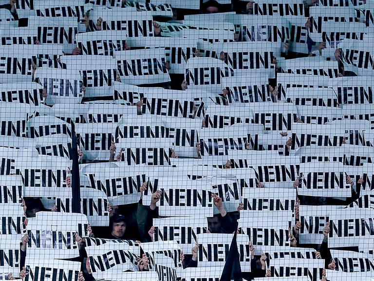 Fußballfans halten Schilder als Protest gegen die Pläne des Bundesinnenministers mit der Aufschrift „NEIN“ vor ihre Gesichter (Borussia-Park Mönchengladbach, 28.11.2025)