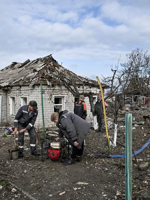 Menschen beugen sich in mitten zerstörter Häuser über einen Generator (Balabyne, Ukraine, 09.06.2026)