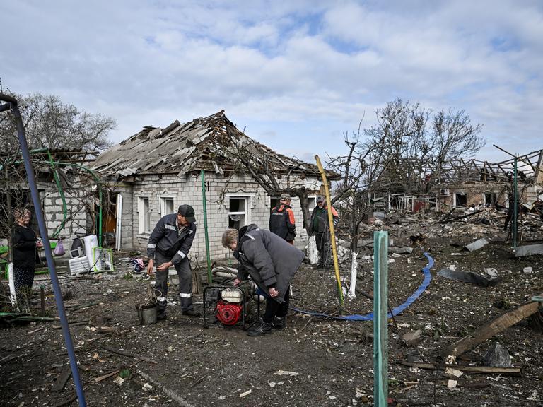 Menschen beugen sich in mitten zerstörter Häuser über einen Generator (Balabyne, Ukraine, 09.06.2026)