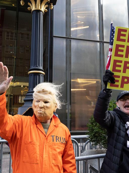 16. November 2025, New York, New York, USA: Ein Mann mit einer Trump-Maske und einem orangefarbenen Gefängnisoverall winkt Passanten auf der Fifth Avenue zu und schließt sich friedlichen Anti-Trump-Demonstranten vor dem Trump Tower an, die Schilder mit… 16. November 2025, New York, New York, USA: Ein Mann mit einer Trump-Maske und einem orangefarbenen Gefängnisoverall winkt Passanten auf der Fifth Avenue zu und schließt sich friedlichen Anti-Trump-Demonstranten vor dem Trump Tower an, die Schilder mit…