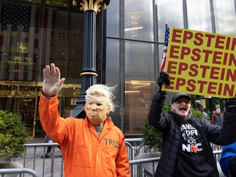 16. November 2025, New York, New York, USA: Ein Mann mit einer Trump-Maske und einem orangefarbenen Gefängnisoverall winkt Passanten auf der Fifth Avenue zu und schließt sich friedlichen Anti-Trump-Demonstranten vor dem Trump Tower an, die Schilder mit… 16. November 2025, New York, New York, USA: Ein Mann mit einer Trump-Maske und einem orangefarbenen Gefängnisoverall winkt Passanten auf der Fifth Avenue zu und schließt sich friedlichen Anti-Trump-Demonstranten vor dem Trump Tower an, die Schilder mit…