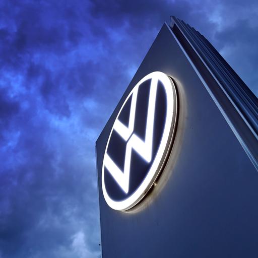 Das Volkswagen-Logo auf einer Steele vor dunklem Himmel mit vielen Wolken.