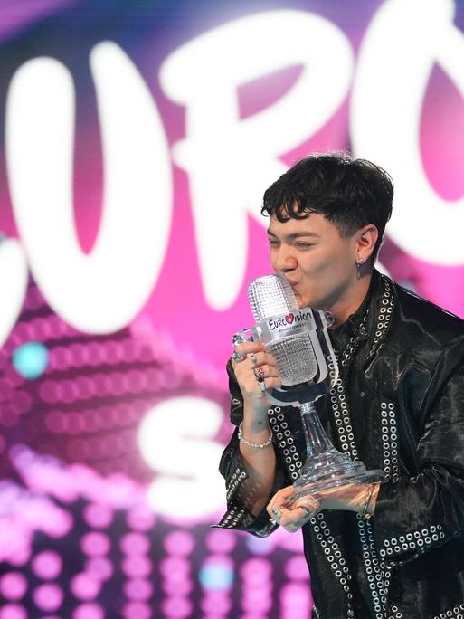 Der österreichische Sänger JJ steht auf der Bühne des ECS 2025, er ist der Gewinner. JJ hält die Gewinner-Trophäe in der Hand und küsst sie; die Trophäe st eine gläserne, mikrofonförmige Statue.