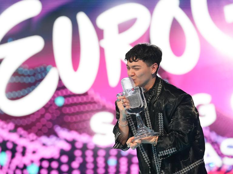 Der österreichische Sänger JJ steht auf der Bühne des ECS 2025, er ist der Gewinner. JJ hält die Gewinner-Trophäe in der Hand und küsst sie; die Trophäe st eine gläserne, mikrofonförmige Statue.