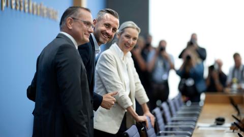 Das Bild zeigt die AfD-Vertreter von der Seite. Sie stehen vor Stühlen vor einem langen Tisch. Im Hintergrund sind der Schriftzug "Bundespressekonferenz" und mehrere Journalisten zu erahnen.