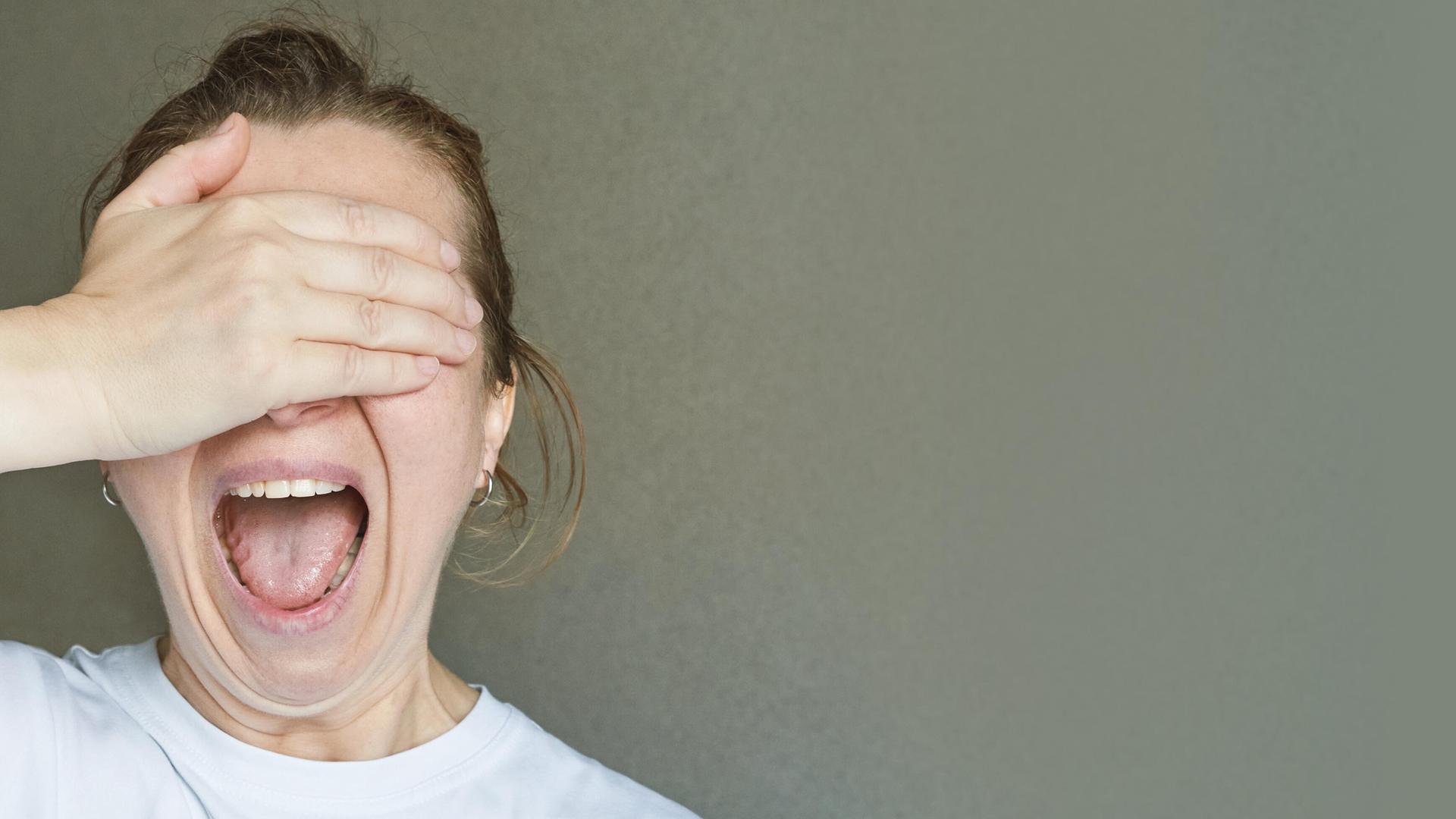 Eine Frau hält sich die rechte Hand vor den Kopf und öffnet den Mund