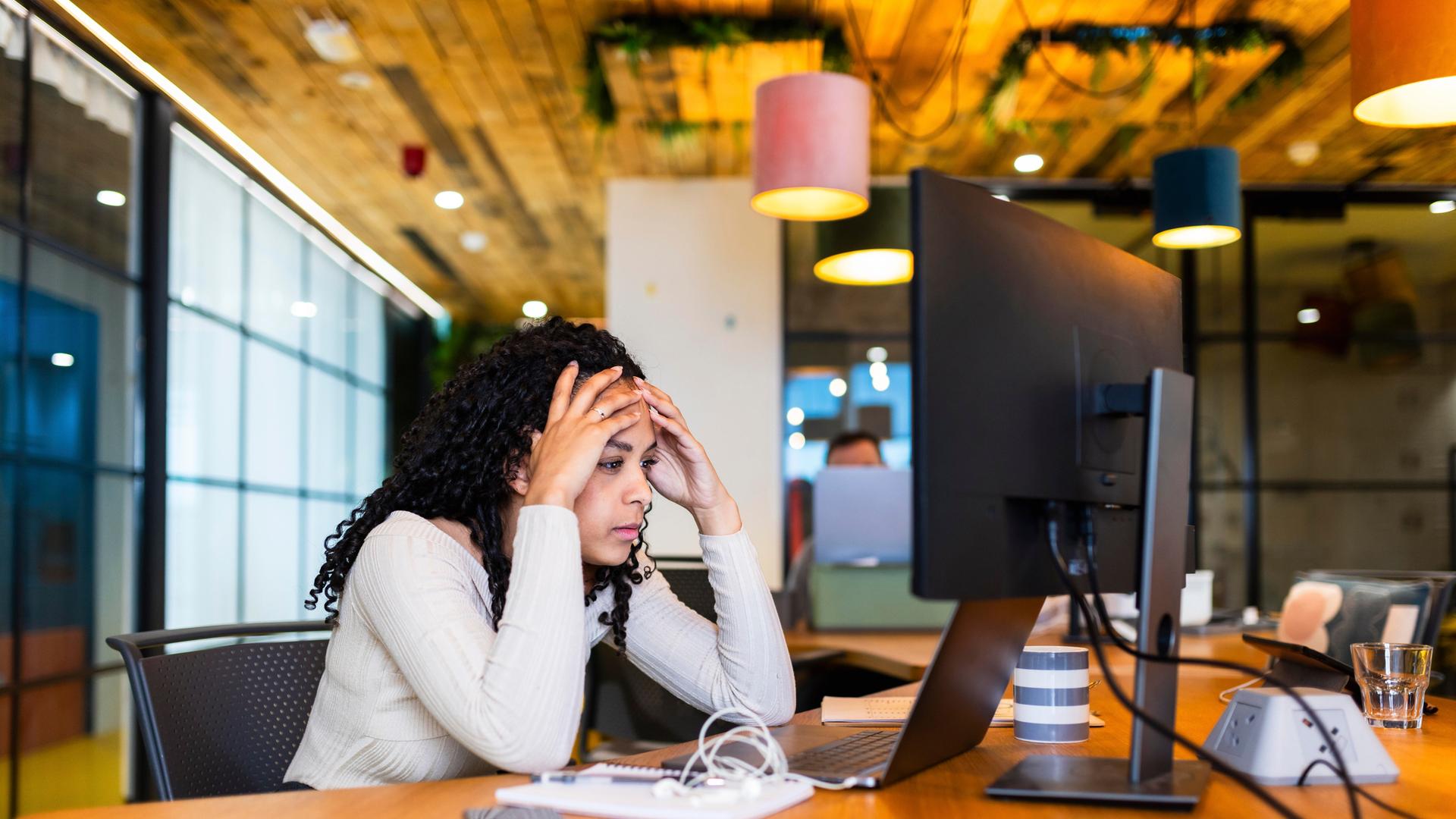 Eine Frau im Büro schaut erschöpft auf einen PC