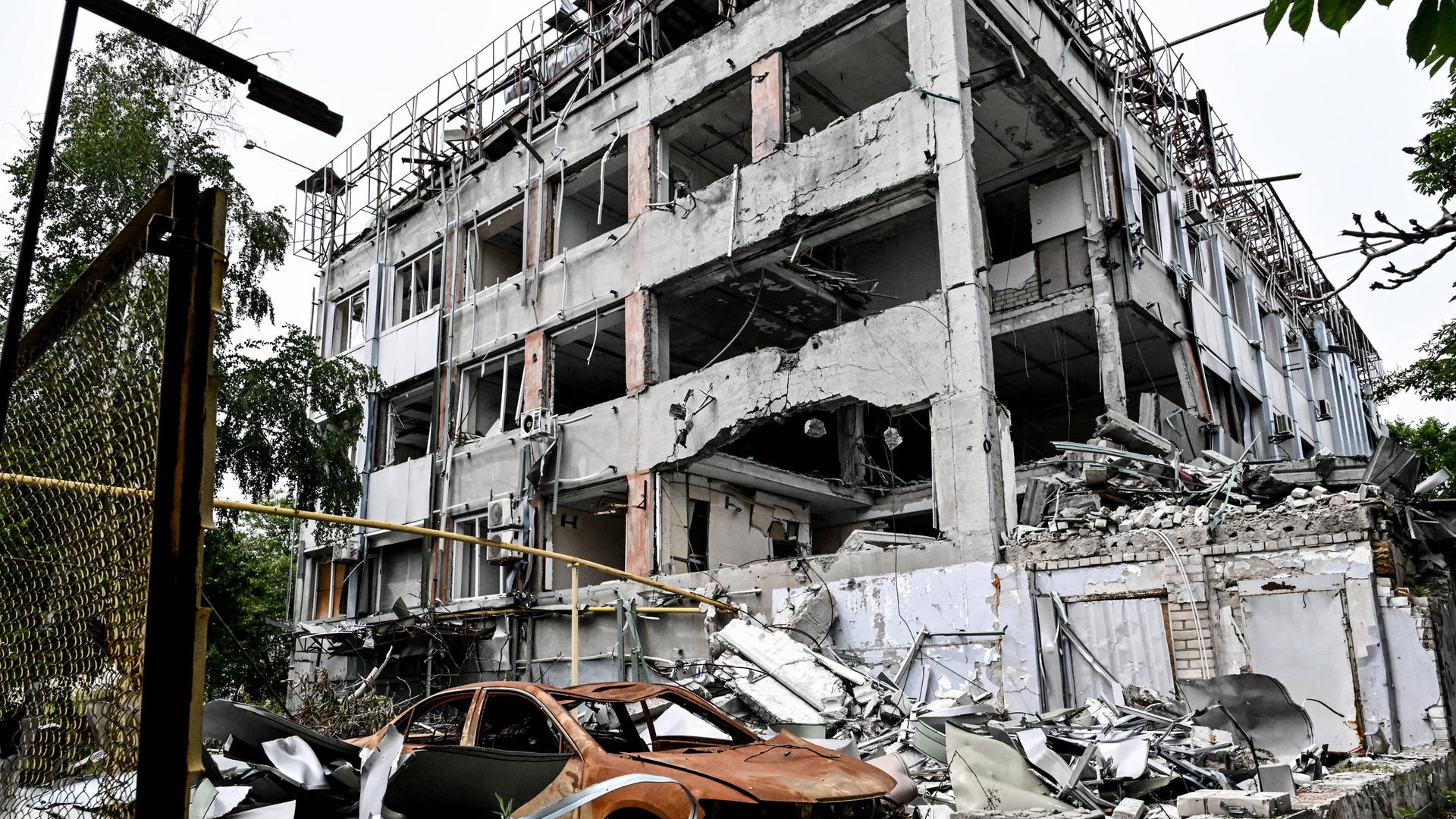Durch russische Angriffe zerstörtes mehrstöckiges Wohnhaus und ausgebranntes rotes Autowrack (10.06.2026) Durch russische Angriffe zerstörtes mehrstöckiges Wohnhaus und ausgebranntes rotes Autowrack (10.06.2026)