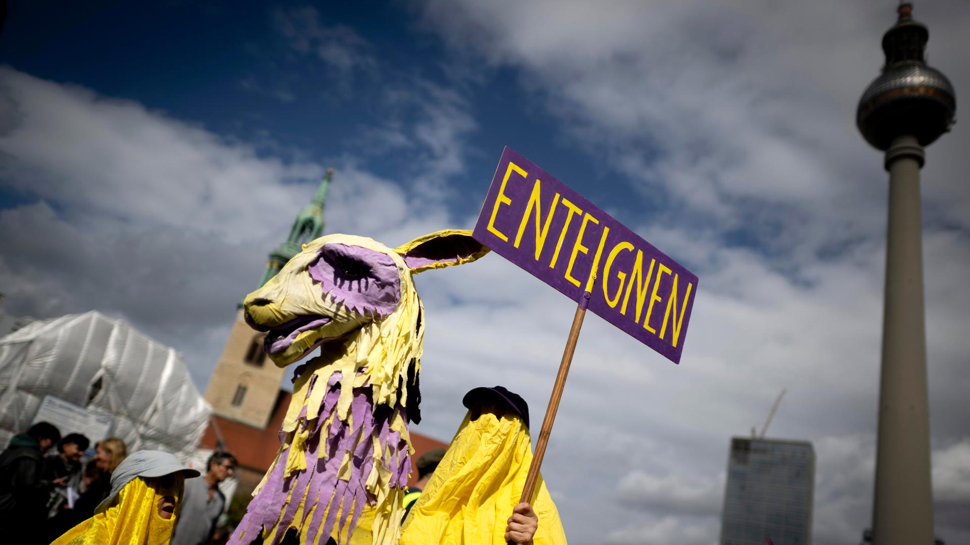 Demonstrant der Initiative Volksentscheid Deutsche Wohnen und Co ist als lila-gelbes Einhorn oder Trojanisches Pferd verkleidet und hält ein Schild mit dem Wort "Enteignung" in die Höhe (05.09.2026, Berlin) Demonstrant der Initiative Volksentscheid Deutsche Wohnen und Co ist als lila-gelbes Einhorn oder Trojanisches Pferd verkleidet und hält ein Schild mit dem Wort "Enteignung" in die Höhe (05.09.2026, Berlin)