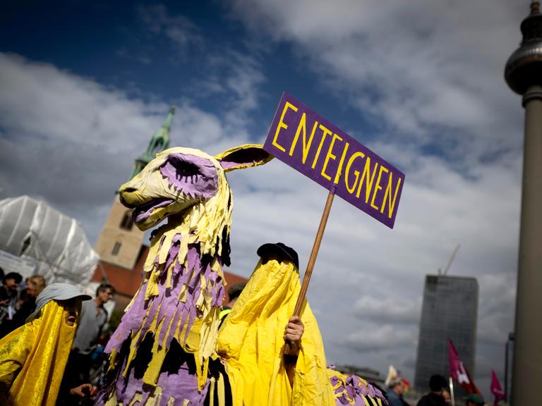 Demonstrant der Initiative Volksentscheid Deutsche Wohnen und Co ist als lila-gelbes Einhorn oder Trojanisches Pferd verkleidet und hält ein Schild mit dem Wort "Enteignung" in die Höhe (05.09.2026, Berlin)