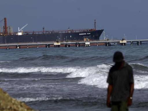 Ein Mann spaziert am Strand von El Palito entlang, im Hintergrund ist die Raffinerie zu sehen, der unter panamaischer Flagge fahrende Öltanker Morning Sun am Dock der Raffinerie El Palito in Puerto Cabello, Bundesstaat Carabobo.