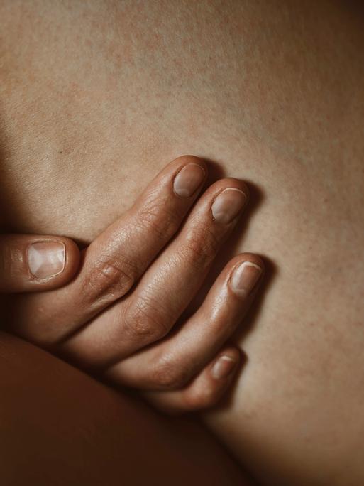 Eine Hand berührt einen nackten Oberschenkel. Das Bild zeigt eine Nahaufnahme. Eine Hand berührt einen nackten Oberschenkel. Das Bild zeigt eine Nahaufnahme.