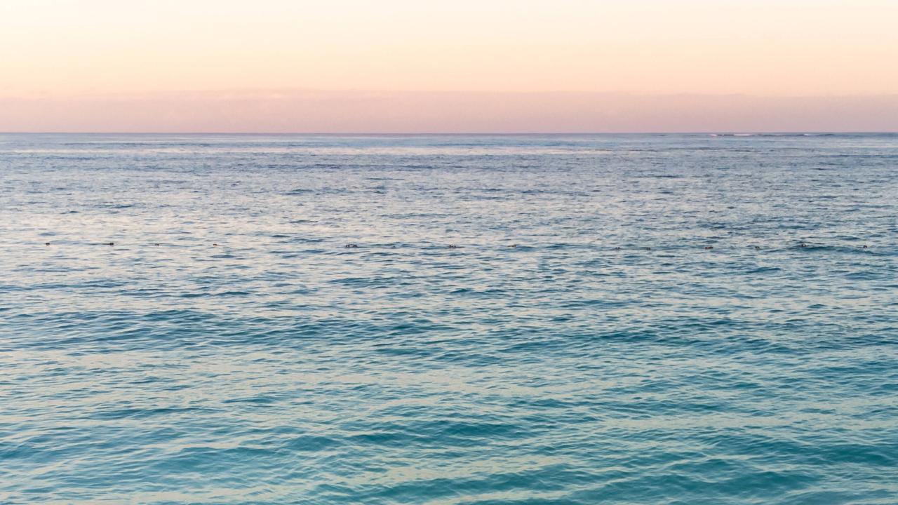 Das Bild zeigt die Wasseroberfläches eines Meers. Am Horizont färbt sich der Himmel orange und rot.