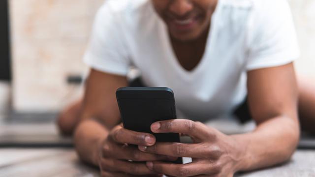Foto eines jungen Mannes, der auf dem Fußboden liegend auf ein Smartphone guckt
