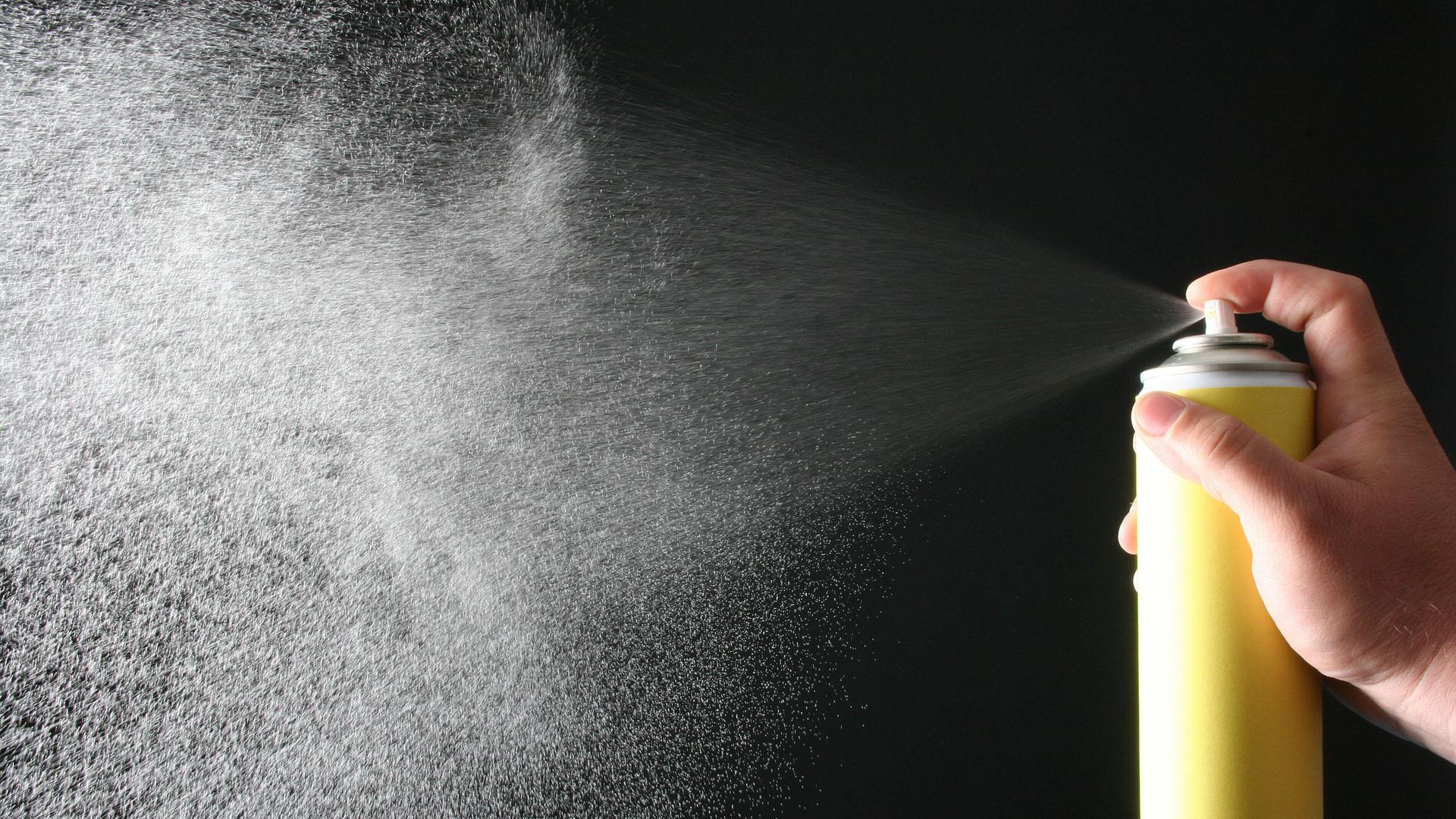 Eine Hand hält eine gelbfarbene Spraydose und sprayt. Der Sprühnebel ist gut erkennbar. Eine Hand hält eine gelbfarbene Spraydose und sprayt. Der Sprühnebel ist gut erkennbar.