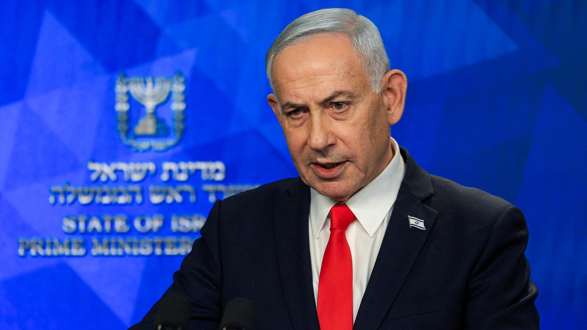 Israels Premierminister Benjamin Netanjahu spricht bei einer Pressekonferenz; er steht in dunklem Anzug, weißem Hemd und roter Krawatte vor einer blauen Wand. Israels Premierminister Benjamin Netanjahu spricht bei einer Pressekonferenz; er steht in dunklem Anzug, weißem Hemd und roter Krawatte vor einer blauen Wand.