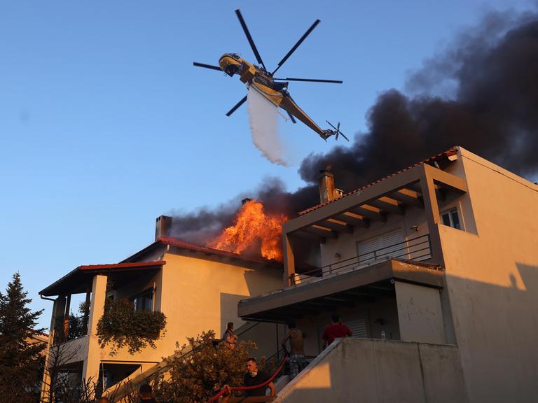 Ein Lösch-Helikopter kippt Wasser über einem brennenden Haus aus