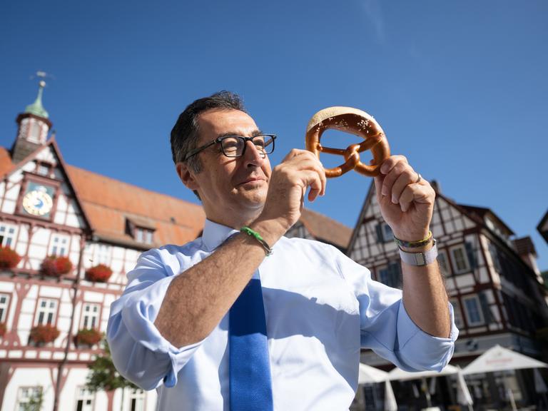 Bundesernährungsminister Cem Özdemir (Bündnis 90/Die Grünen) zeigt auf dem Marktplatz seines Geburtsorts nach dem Besuch einer Bäckerei eine Brezel.