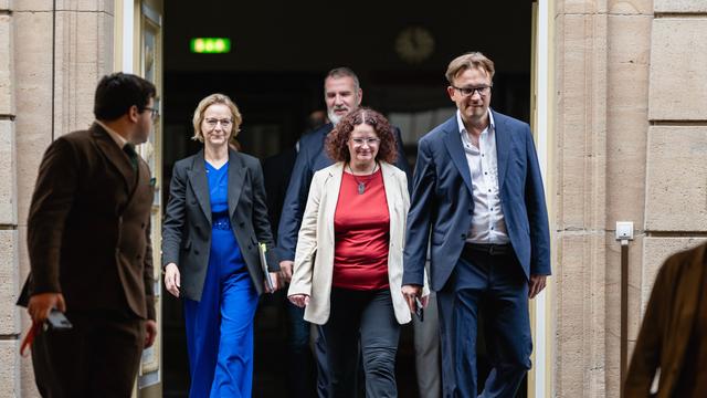 Mehrere Menschen in Anzügen laufen aus einer Tür raus.