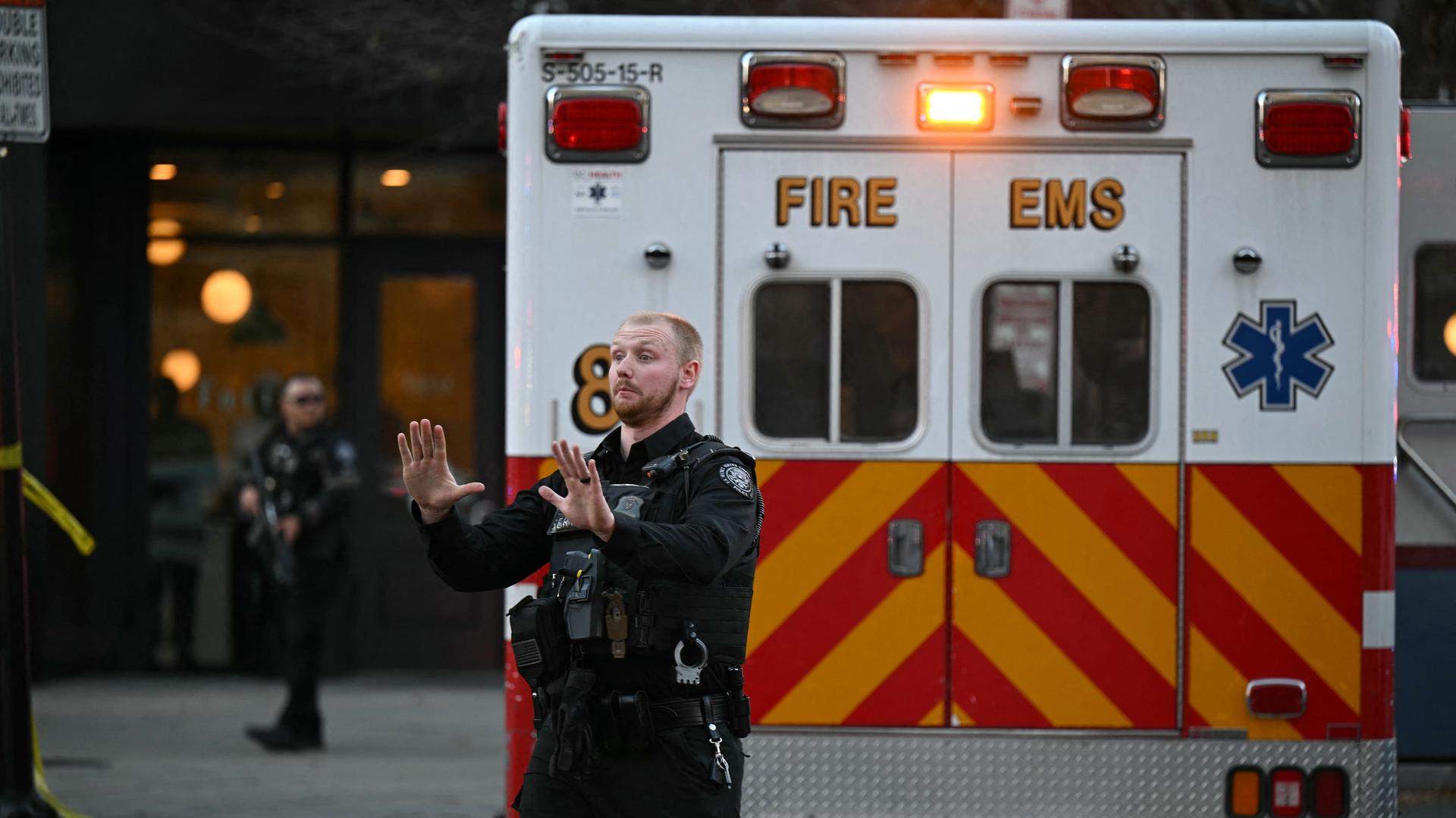Ein amerikanischer Polizist steht vor einem Krankenwagen und gestikuliert. Die Türen des Fahrzeugs sind geschlossen. Nur seine Rückseite ist zu sehen.