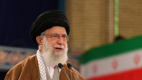 Das Foto zeigt einen älteren Mann, im Hintergrund die iranische Flagge