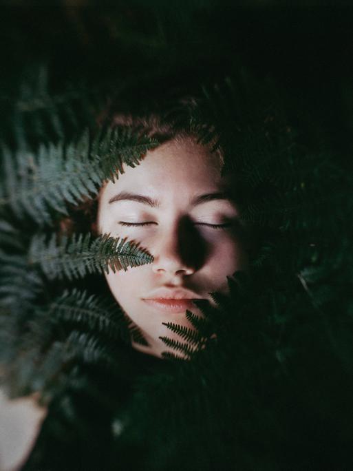 Das Gesicht eines jungen Menschen im Vordergrund ein Farn