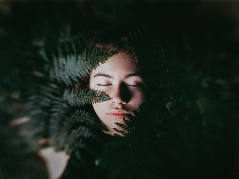 Das Gesicht eines jungen Menschen im Vordergrund ein Farn