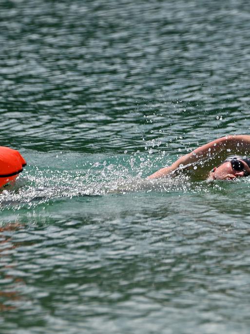 Ein Mann schwimmt im See. Er zieht eine Boje hinter sich her.