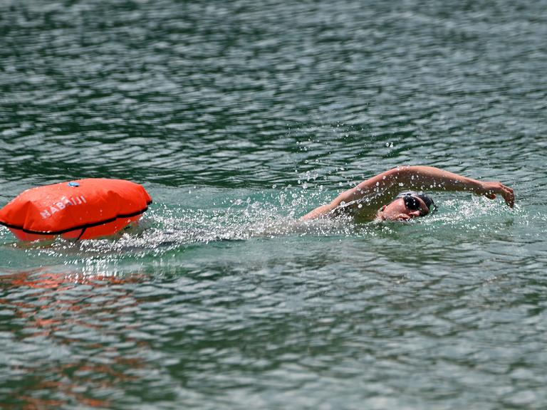 Ein Mann schwimmt im See. Er zieht eine Boje hinter sich her.