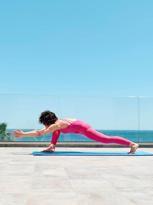 Eine Frau in einem pinken Sportanzug macht Yoga auf einer Dachterrasse