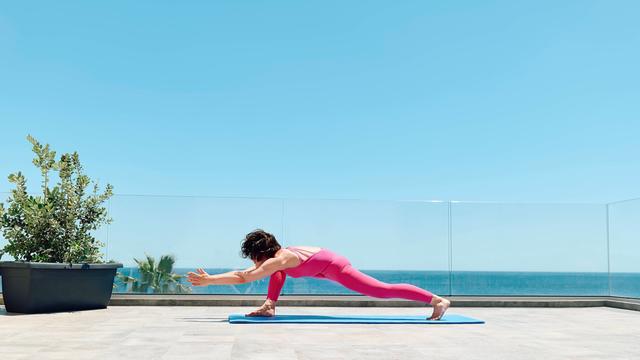 Eine Frau in einem pinken Sportanzug macht Yoga auf einer Dachterrasse