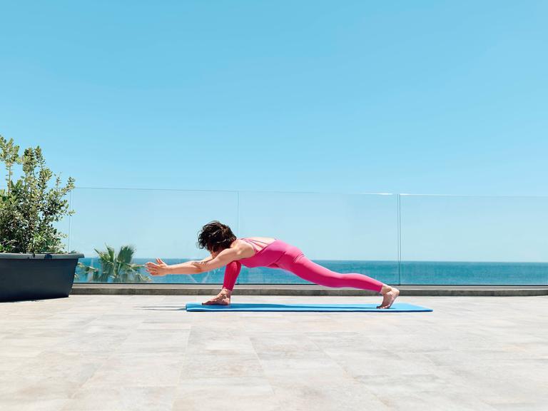 Eine Frau in einem pinken Sportanzug macht Yoga auf einer Dachterrasse