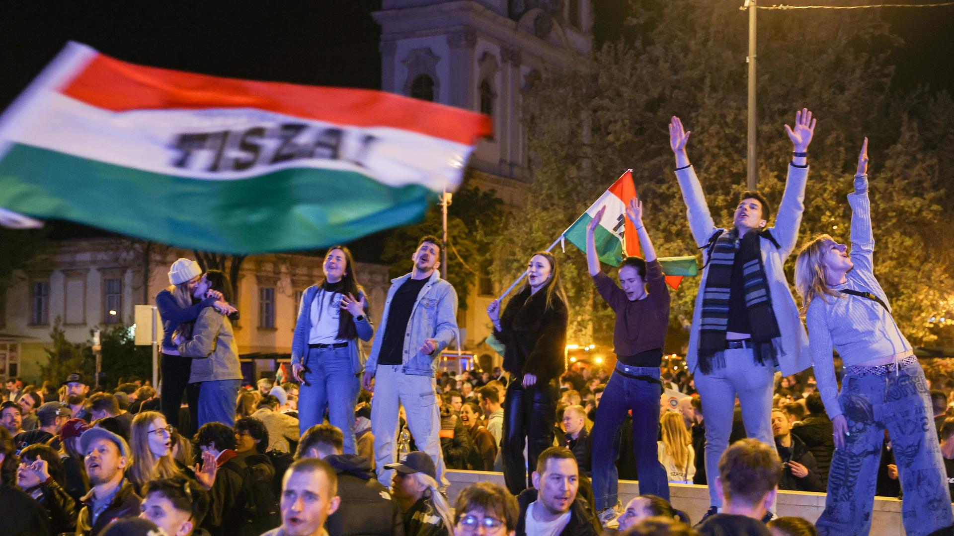 Junge Leute stehen auf einer Mauer und schwenken Ungarn-Flaggen nach dem Wahlsieg von Péter Magyar (Budapest 13.04.2026) Junge Leute stehen auf einer Mauer und schwenken Ungarn-Flaggen nach dem Wahlsieg von Péter Magyar (Budapest 13.04.2026)