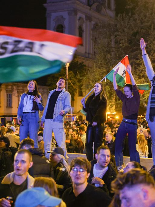 Junge Leute stehen auf einer Mauer und schwenken Ungarn-Flaggen nach dem Wahlsieg von  Péter Magyar (Budapest 13.04.2026)
