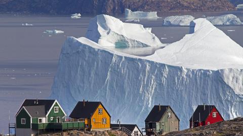 Grönländische Holzhäuser vor Eisberg im Hintergrund