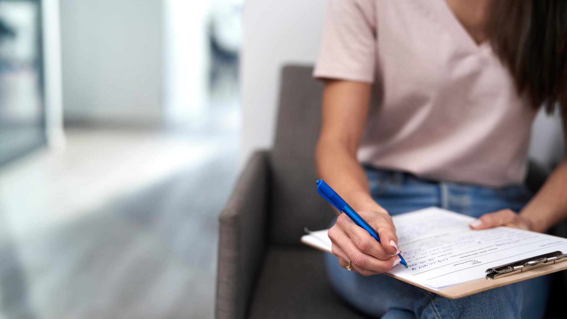 Frau sitzt im Wartezimmer und füllt ein Formular aus