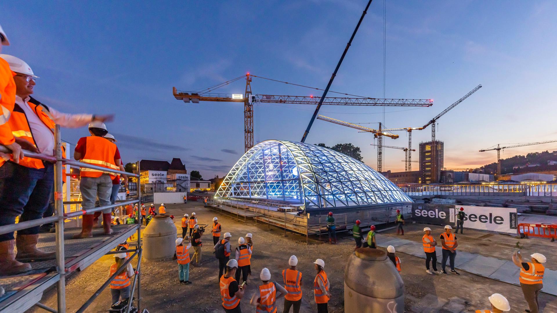 Auf der Baustelle von Stuttgart 21 ist ein großes Glasdach zu sehen, außerdem mehrere Baukräne und Bauarbeiter.
