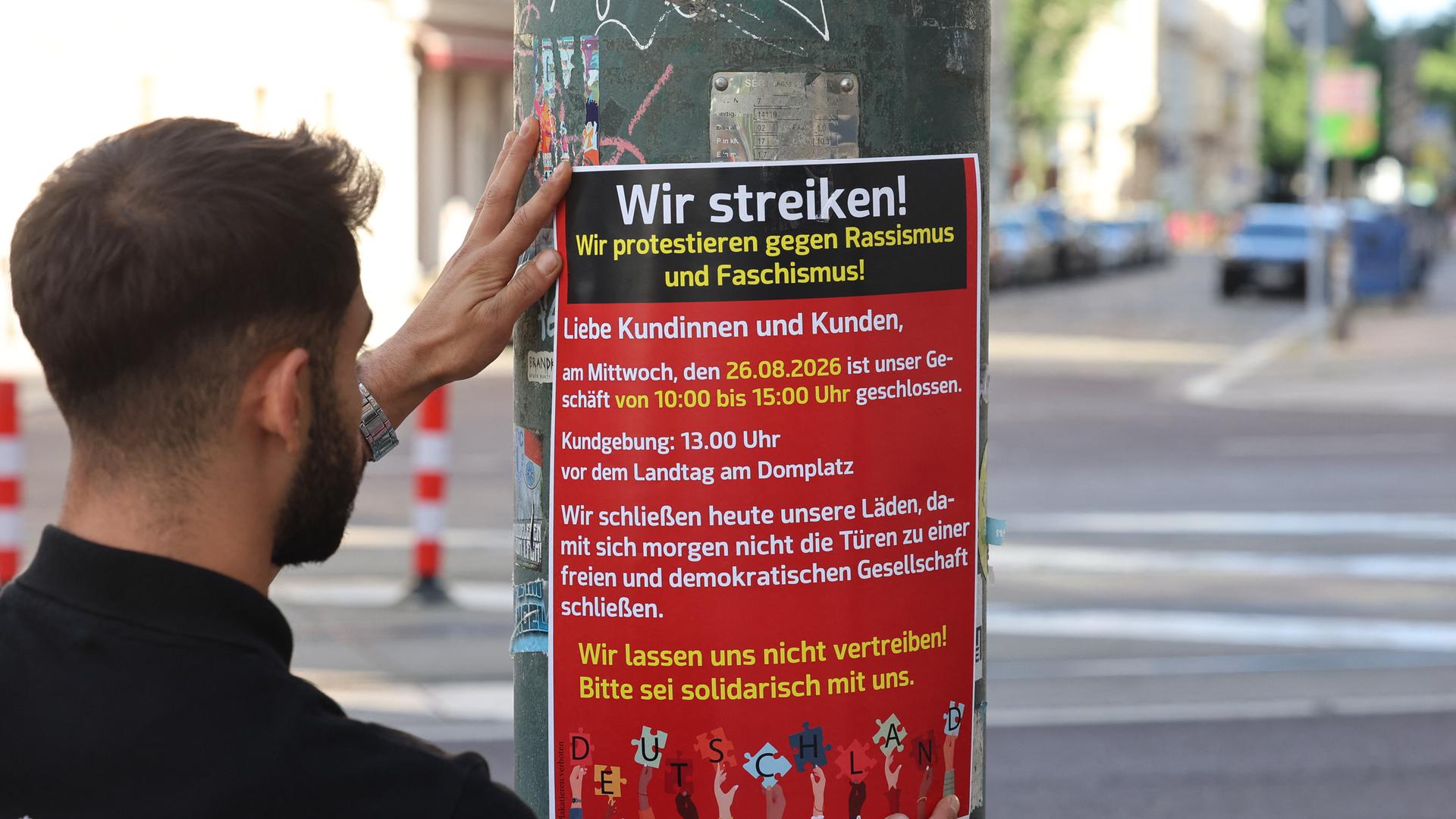 Mann bringt ein Plakat an, das zum "Migra-Streik" aufruft (Magdeburg, 25.08.2026)