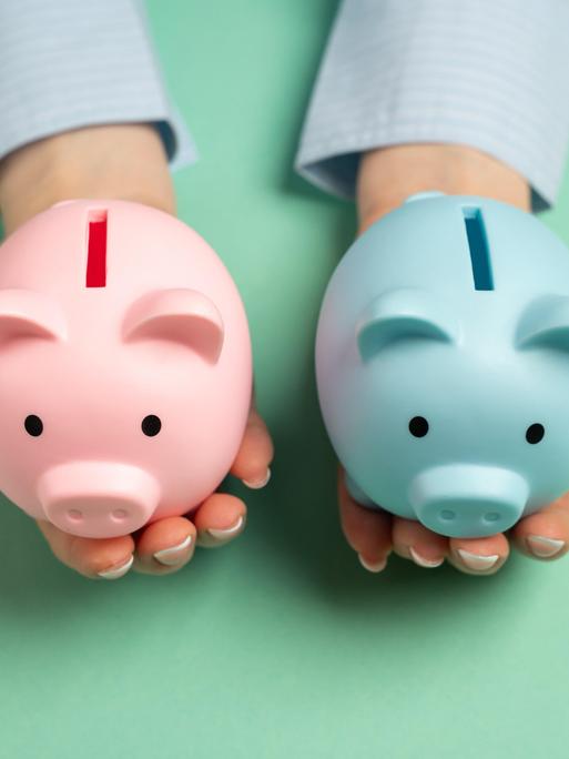 Symbolbild: Ein rosanes und ein blaues Sparschweinchen, die den Gender Pay Gap symbolisieren