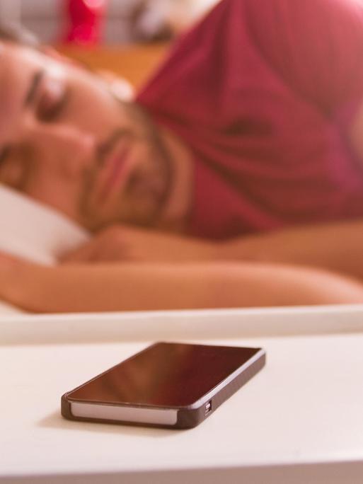 Ein Mann im Bett, vor ihm ein Smartphone