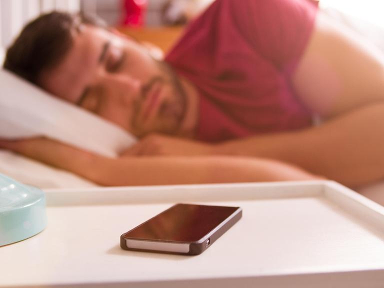 Ein Mann im Bett, vor ihm ein Smartphone