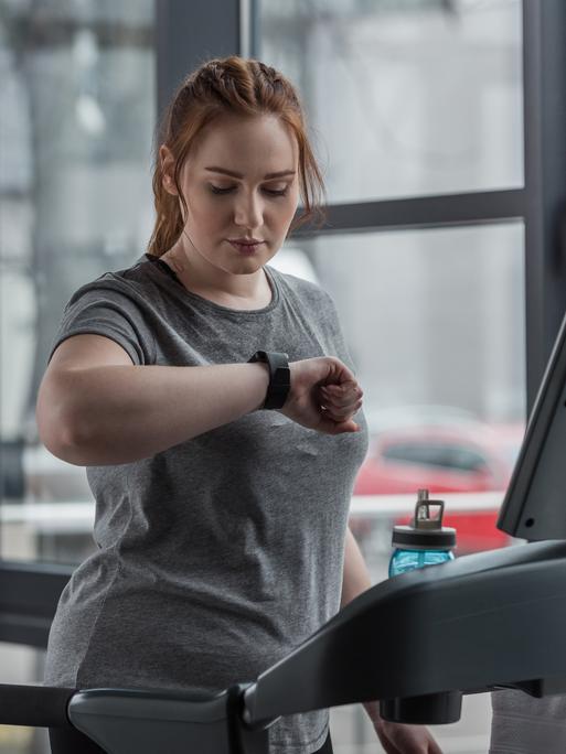 Eine Frau auf einem Laufband schaut auf ihren Fitnesstracker Eine Frau auf einem Laufband schaut auf ihren Fitnesstracker