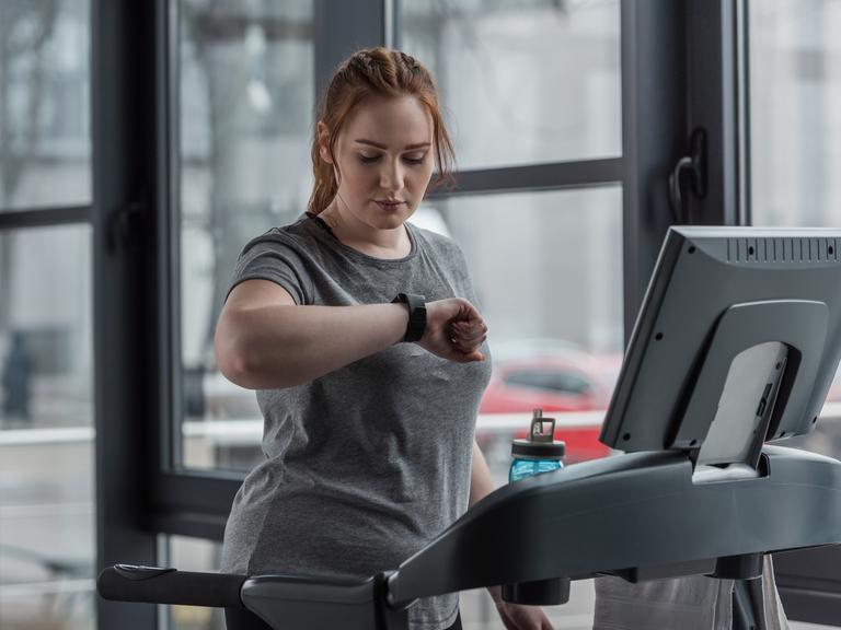 Eine Frau auf einem Laufband schaut auf ihren Fitnesstracker Eine Frau auf einem Laufband schaut auf ihren Fitnesstracker