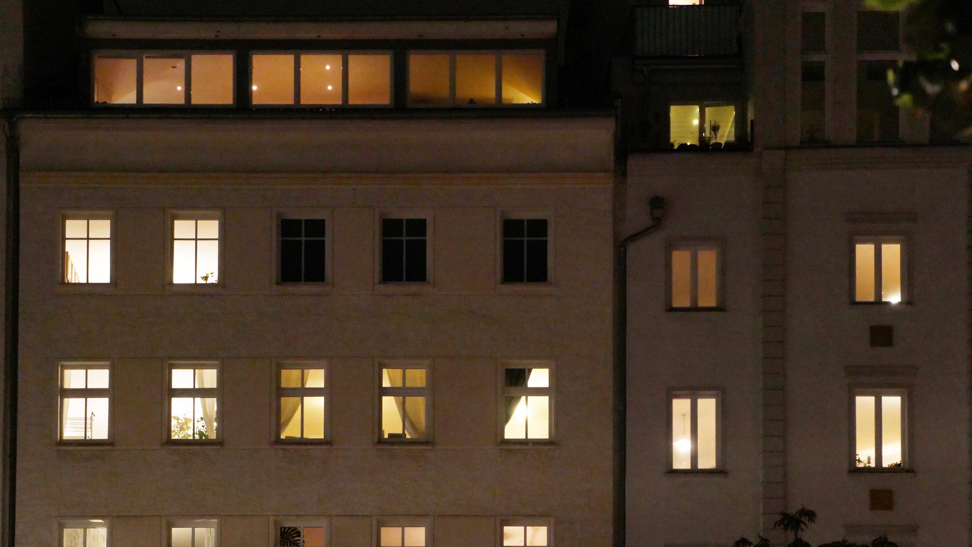 Ein Mehrfamilienhaus am Abend. Die meisten Fenster sind erleuchtet.