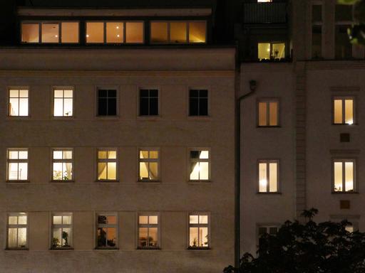 Ein Mehrfamilienhaus am Abend. Die meisten Fenster sind erleuchtet.