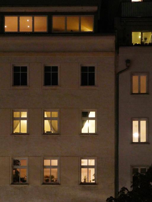 Ein Mehrfamilienhaus am Abend. Die meisten Fenster sind erleuchtet.