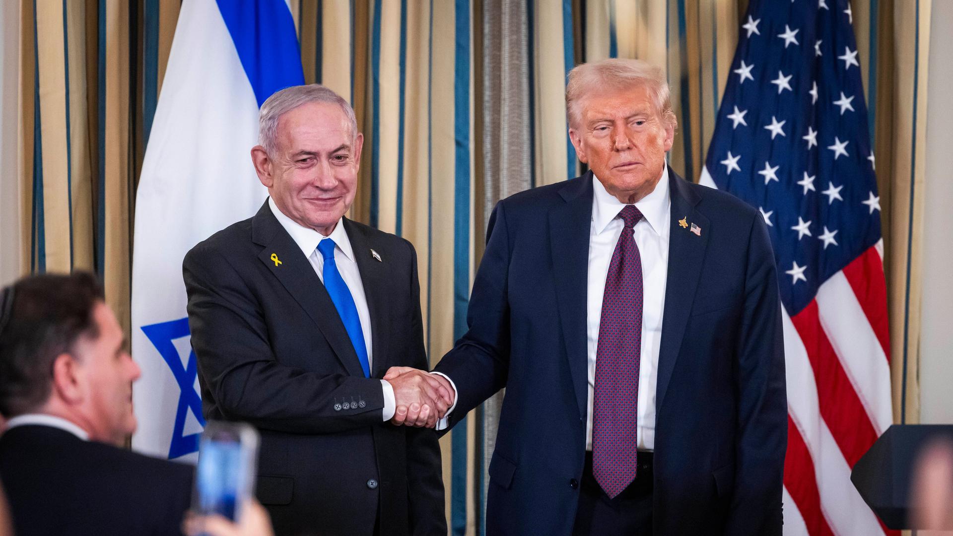 Benjamin Netanjahu und Donald Trump reichen sich die Hand, nachdem der israelische Premier ankündigte, dem Friedensplan zuzustimmen. Im Hintergrund die Flaggen Israels und der USA. Benjamin Netanjahu und Donald Trump reichen sich die Hand, nachdem der israelische Premier ankündigte, dem Friedensplan zuzustimmen. Im Hintergrund die Flaggen Israels und der USA.